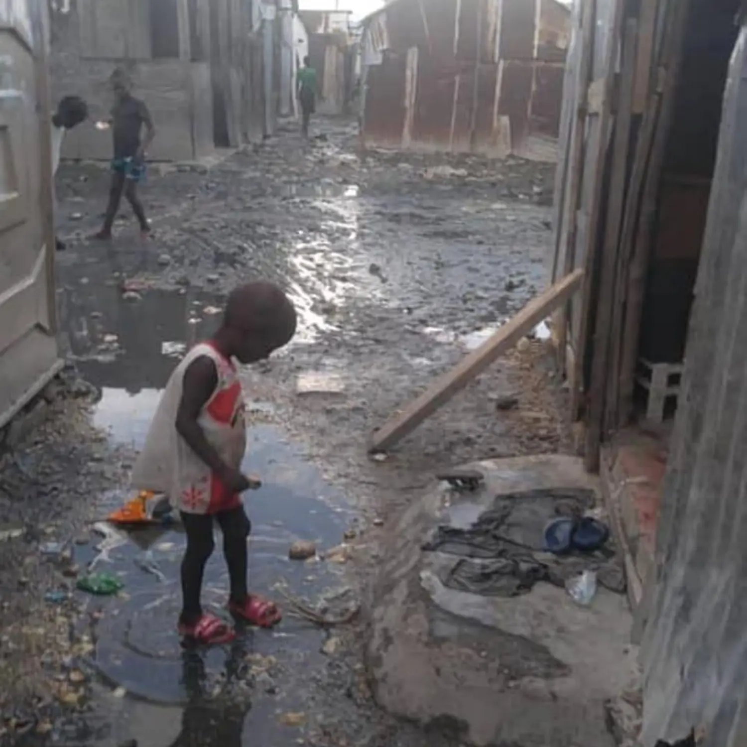 Seven4ONE - ein afrikanisches Kind außerhalb des Tierheims, das in eine Wasserpfütze springt